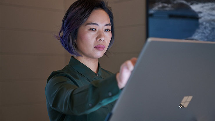 Side profile of a woman wearing a dark shirt in a dim office reaching up and working on a Microsoft Surface Studio.