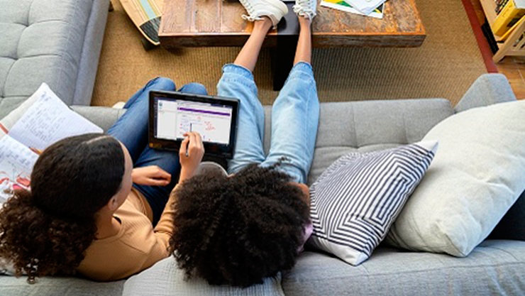 Two K-12 students sit together on a sofa using Microsoft Teams