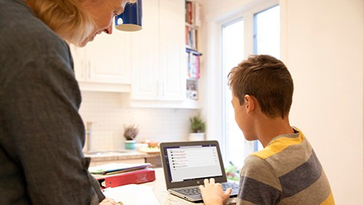 A K-12 student works on device with adult standing next to them.