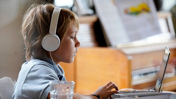A K-12 student sits with headphones on working on a device