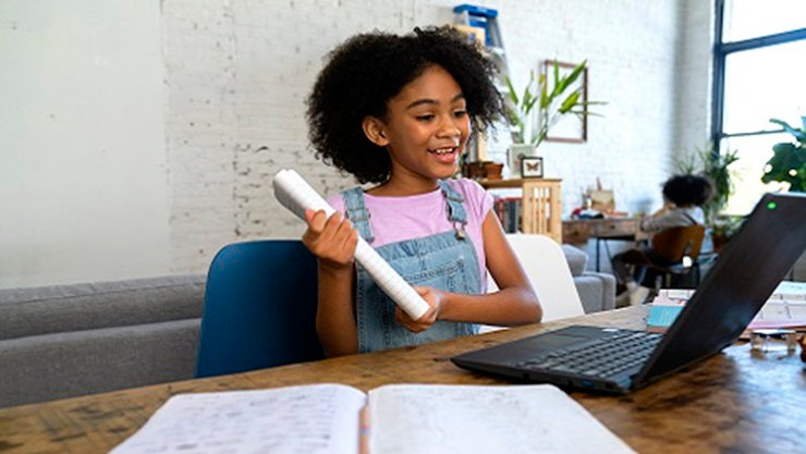 K-12 student at home, using Microsoft Teams on an Acer Travelmate Spin B3 for remote learning. A sibling is in the background, also engaged in remote learning on a Windows 10 device.