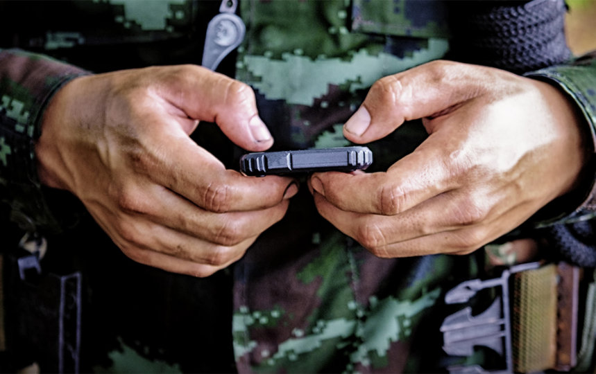 Close up shot of the hands of a man in military uniform typing on a smartphone device