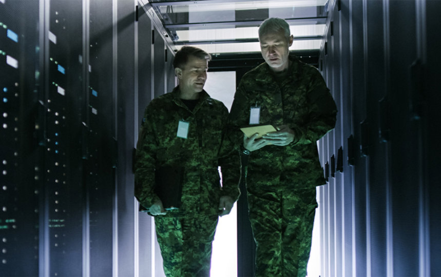 Two men in military uniform walk along a rack of servers