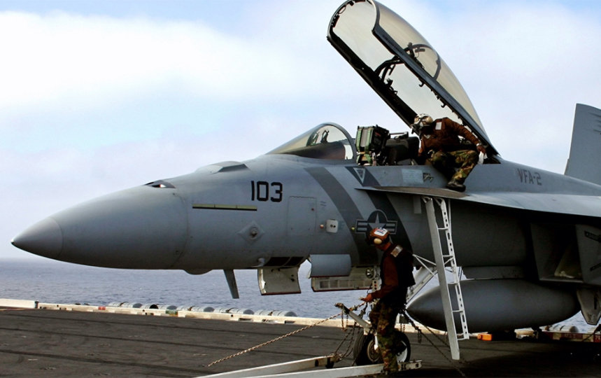 Serviceman walks under a fighter jet on the top of an aircraft carrier