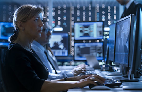 Line of analysts working on monitors to analyze data sit in a control room