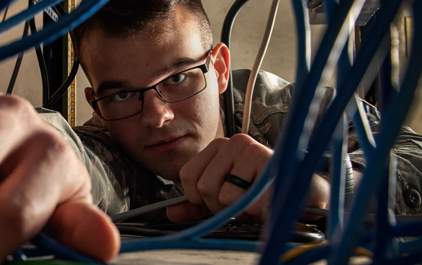 An Air Force man reaching through wires under a desk