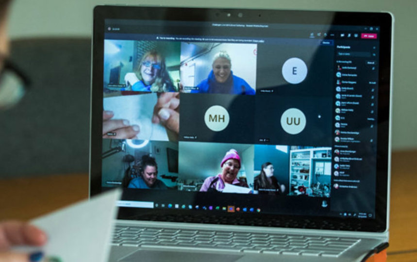 Virtual meeting participant at her desk looking at a screen with fellow participants 