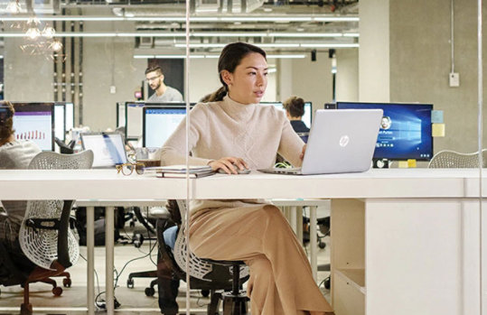 Woman works at her HP laptop in a modern, open concept office.