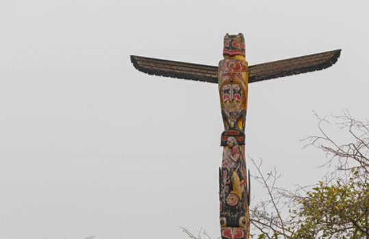 Indigenous totem pole stands tall above a forest enveloped in fog.
