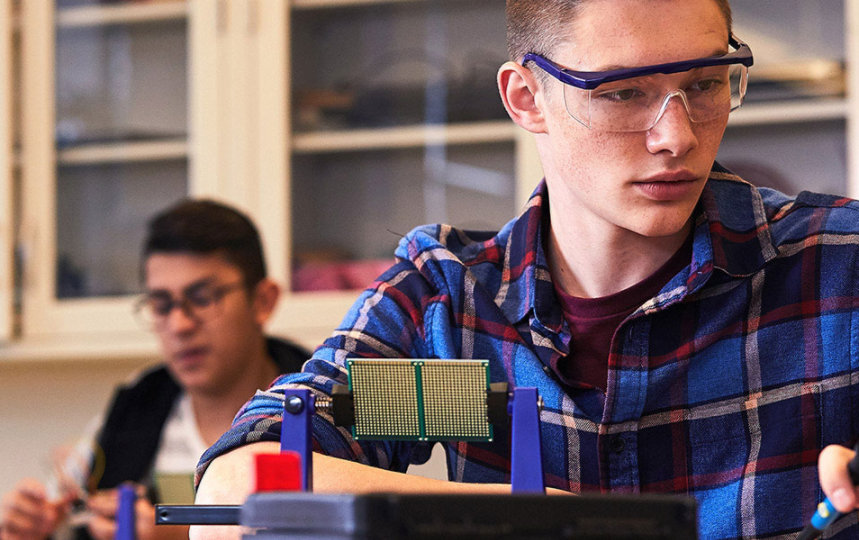 Two students in safety glasses work on a robotics project in their science classroom