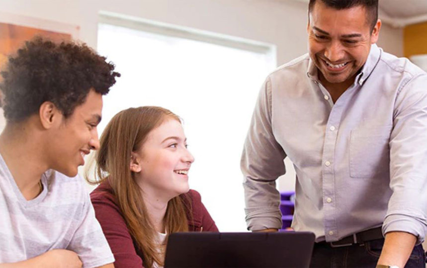 Two high school students and their teacher gather around a laptop in their classroom