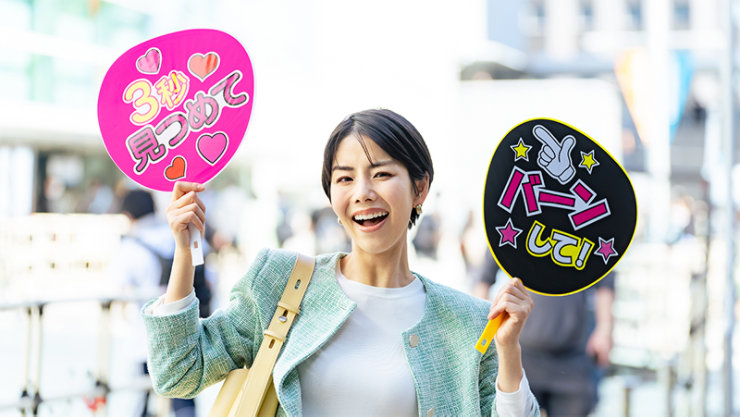  屋外イベントで日本語が書かれたカラフルなハート型と丸型のうちわを持って笑顔の若い女性。
