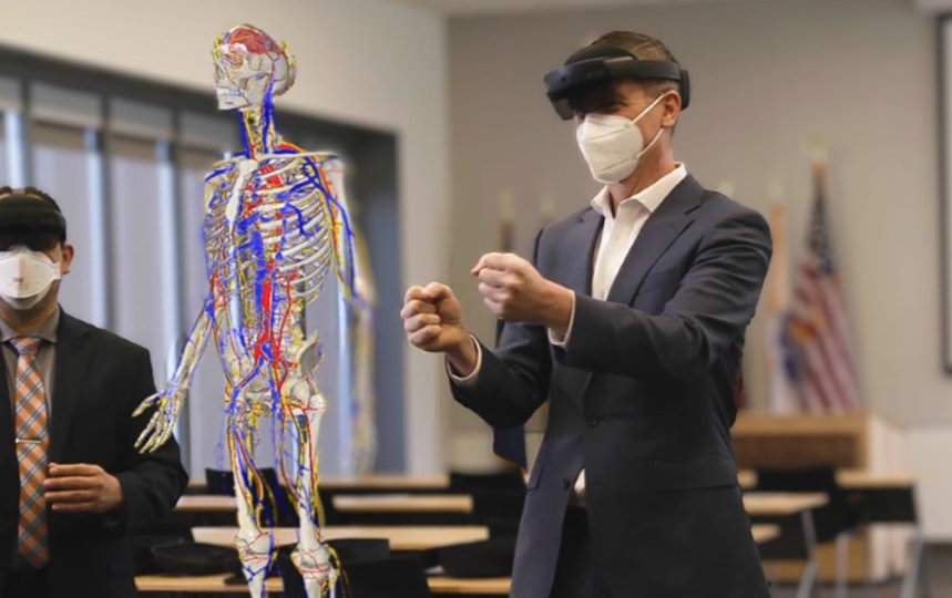 3 business professionals use mixed-reality headsets in a classroom to collaborate on viewing a virtual reality skeleton