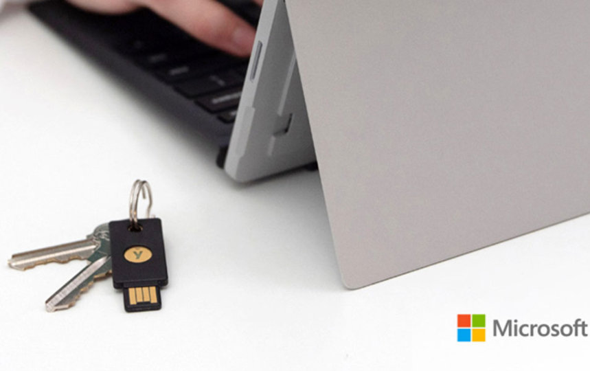 Hands typing on a Microsoft table next to a YubiKey