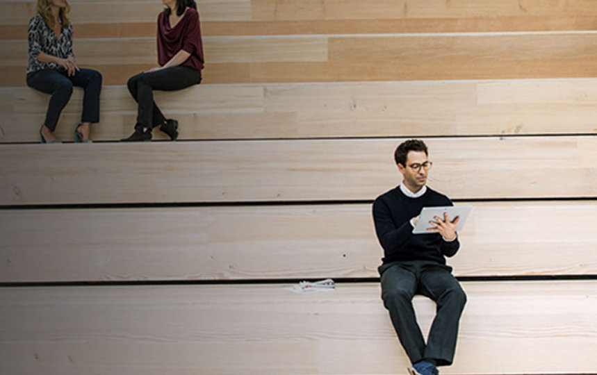 a guy working in his surface device and two women sitting in background on staircases