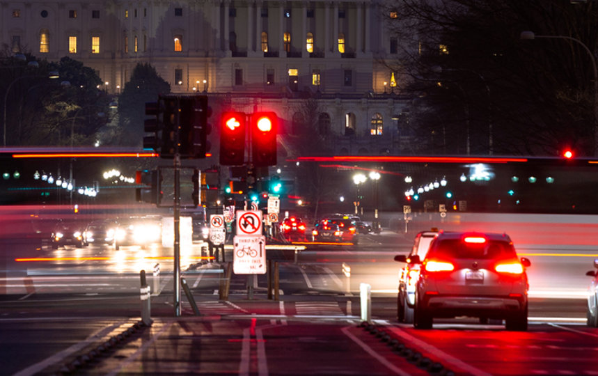cars driving down Pennsylvania Ave at night towards the U.S. Capitol.