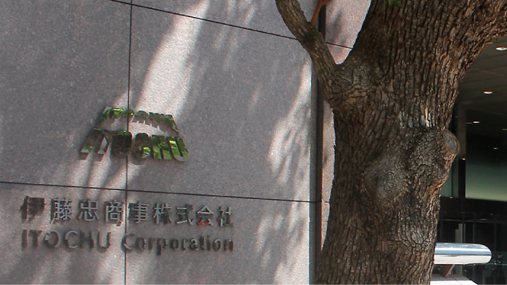 「伊藤忠商事株式会社 ITOCHU Corporation」の社名が刻まれた石造りの外壁と、手前に伸びる大きな木の幹。