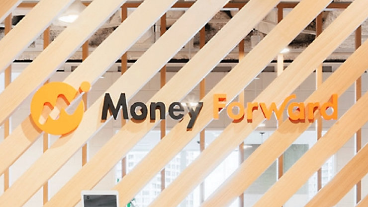 モダンなオフィス内で、明るい木製の格子越しに見える「Money Forward」のロゴ。