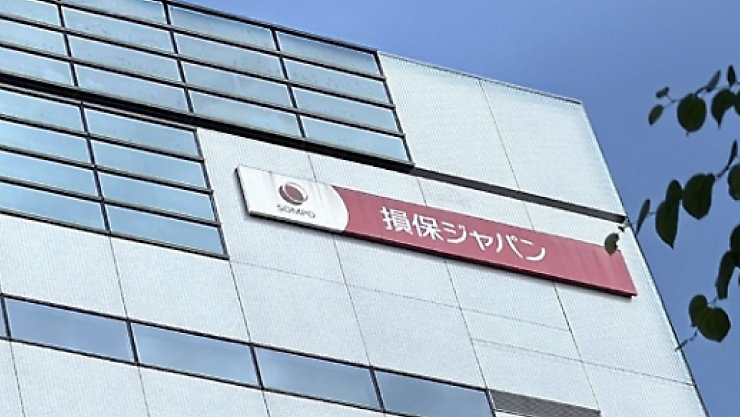 青空を背景に、赤い「損保ジャパン」SOMPO の看板を掲げたオフィスビルの外観。