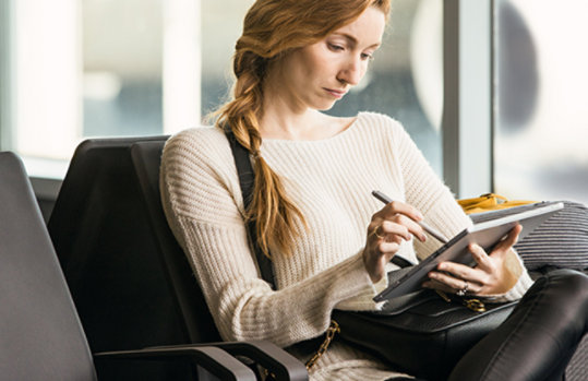 Eine Frau sitzt neben einer Glaswand und bedient ein mobiles Gerät mithilfe eines Pointers
