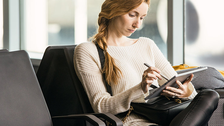 Eine Frau sitzt neben einer Glaswand und bedient ein mobiles Gerät mithilfe eines Pointers