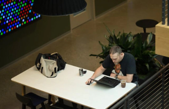Ein Mann sitzt an einem Tisch und blickt auf einen Laptop