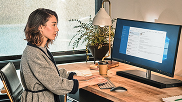 Eine Frau bedient einen Computer auf einem Holztisch, in einem hellen Zimmer
