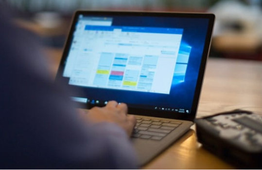 Die Kamera sieht einer Person über die Schulter, die gerade einen Laptop bedient