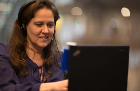 Eine Frau bedient lächelnd einen Laptop, während sie ein Headset trägt