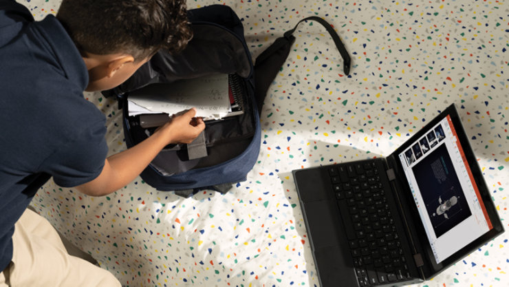 ベッドの上のバックパックに荷物を詰める子どもと横に置いているノート PC