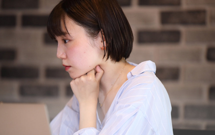 若い女性が手にあごを乗せてノートパソコンの画面に集中しています。