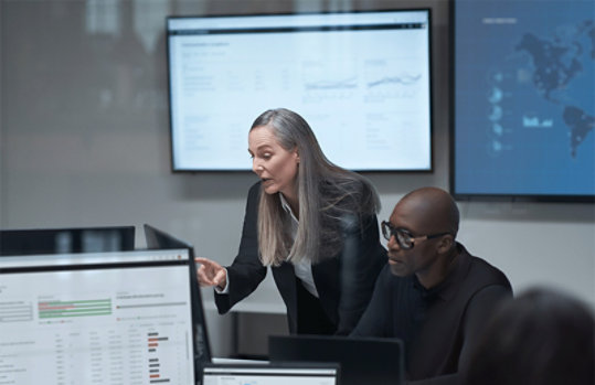 ラップトップで作業し、マルチクラウド環境について発表する女性と男性