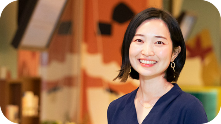 オフィスのような雰囲気で撮影された、笑顔のユカさんのポートレート。