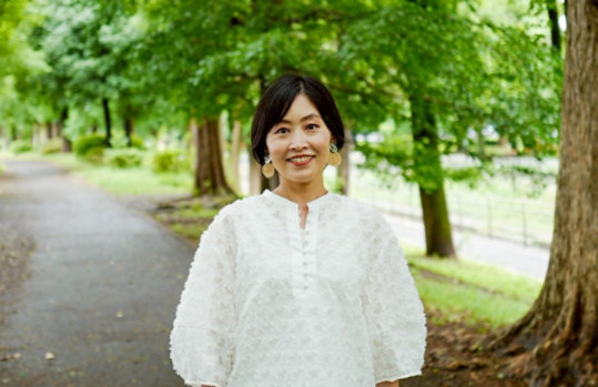 背景に木々が見える屋外で立っているMadoka