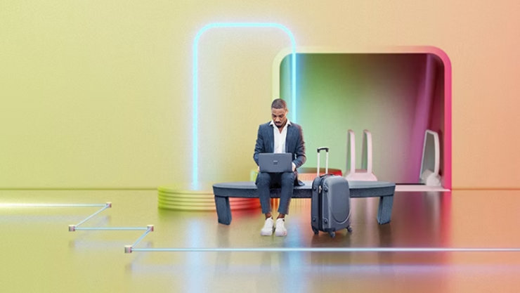 Eine Person sitzt mit einem Koffer auf einer Bank und bedient ein Laptop.