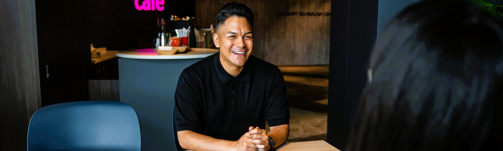 黒いポロシャツを着て、他の社員と話している様子のMauricio