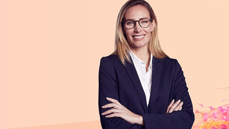 Frau mit Brille, Arme vor der Brust verschrenkt. Orangener Hintergrund