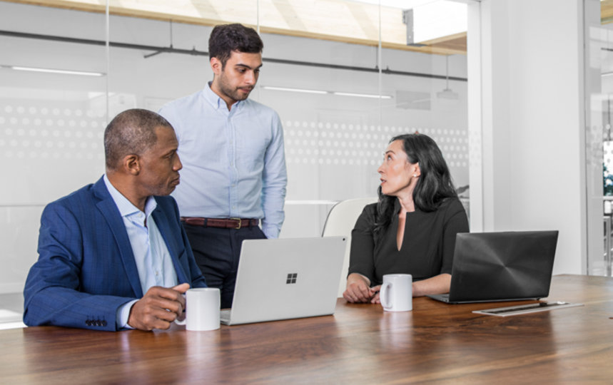 Two male and one female corporate office workers sitting at conference room table in discussion.