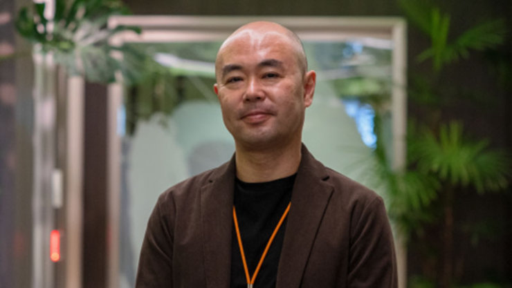 マサキは茶色のジャケットを着ており、背景には植物が描かれています。