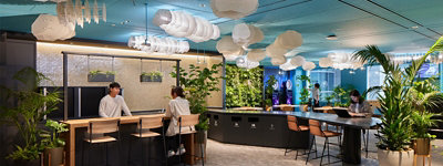 品川オフィスのハブスペースに数名の男女がいて、左側のカウンター越しに話をしている人、その右側のカウンターではPCを操作している人、奥にはダーツをしている人がいる