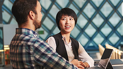 ノート PC が置かれたデスクの前に並んで座って話す 2 人のビジネス パーソン