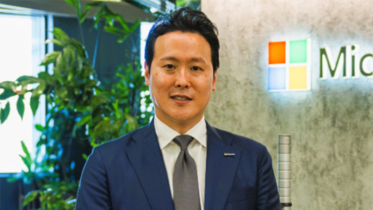 Microsoftのロゴが後ろに見える社内で立っているShota
