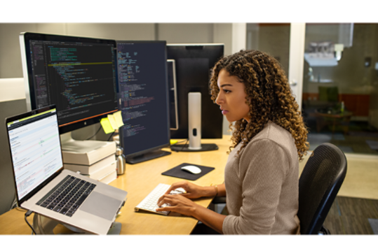 1 台のノート パソコンと 2 つのディスプレイが置かれたデスクでキーボード入力をするビジネス パーソン