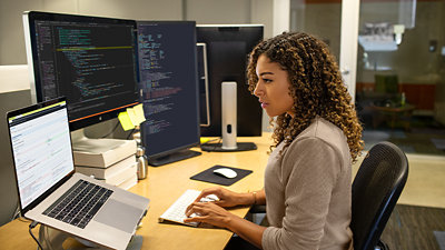 1 台のノート パソコンと 2 つのディスプレイが置かれたデスクでキーボード入力をするビジネス パーソン