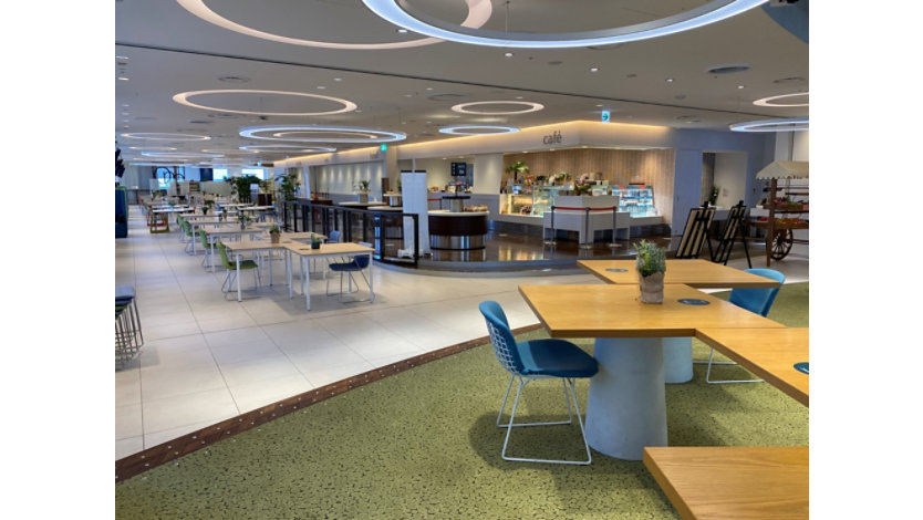 広いカフェテリアにいくつかのテーブルや椅子が置かれている。天井には丸い形の照明