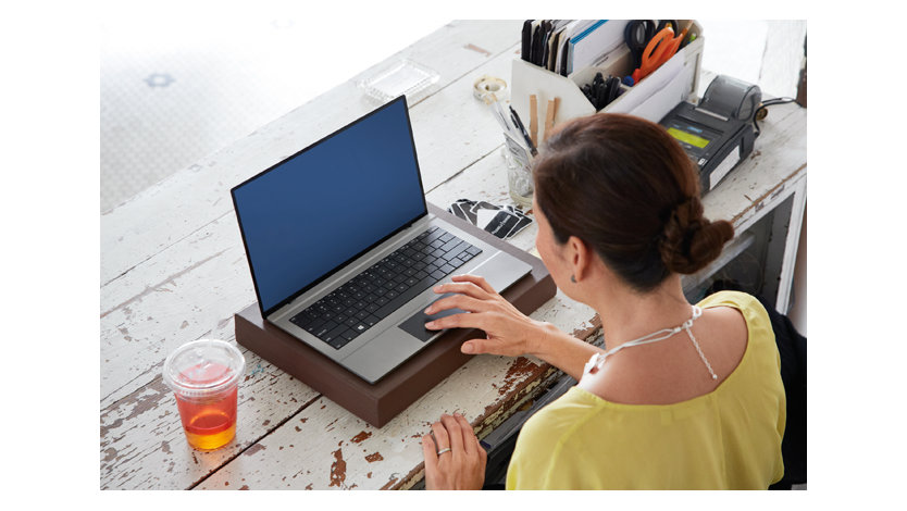 机の上でノートパソコンを作業している黄色いトップの女性