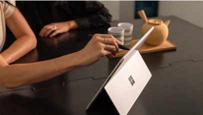 机の上の Surface ノート PC でスタイラスを使って書いている人