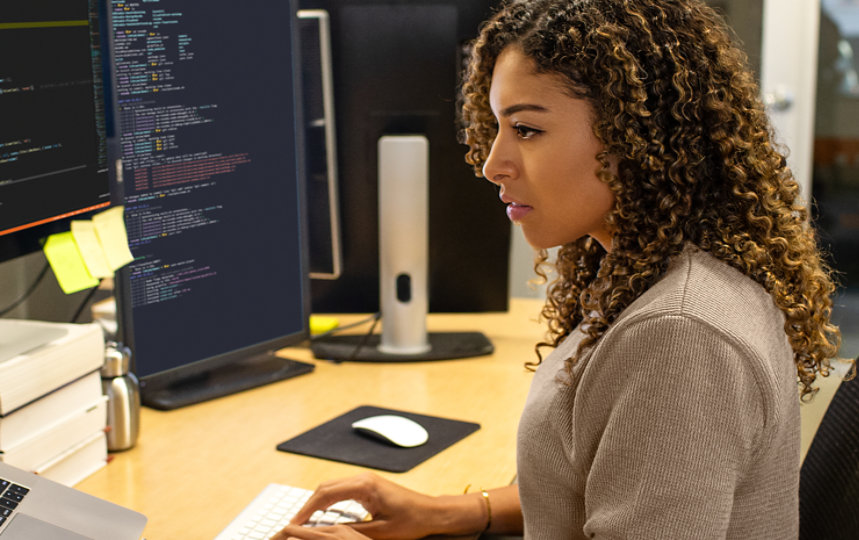 1 台のノート パソコンと 2 つのディスプレイが置かれたデスクでキーボード入力をするビジネス パーソン