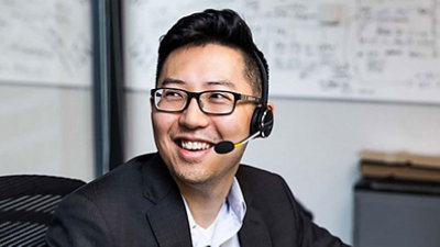 ひとりの男性がパソコンの前に座わり、右を向いて笑顔で話している