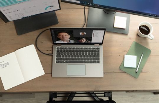 机の上にパソコンやモニター、ペンなどが置かれている。パソコンの画面にはビデオ会議の相手数人の顔が映っている。